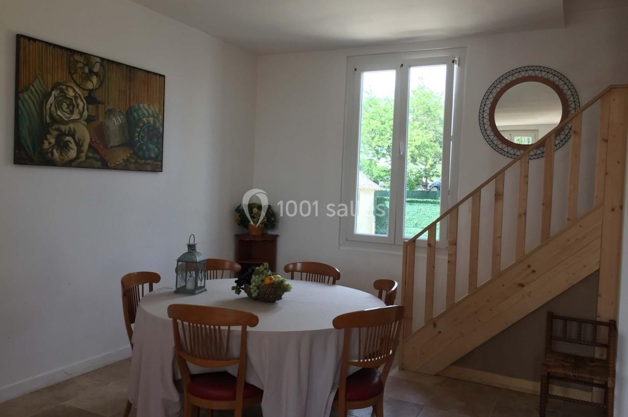 Salle à manger lumineuse avec table ronde, chaises en bois, escalier en bois et fenêtre donnant sur un jardin.