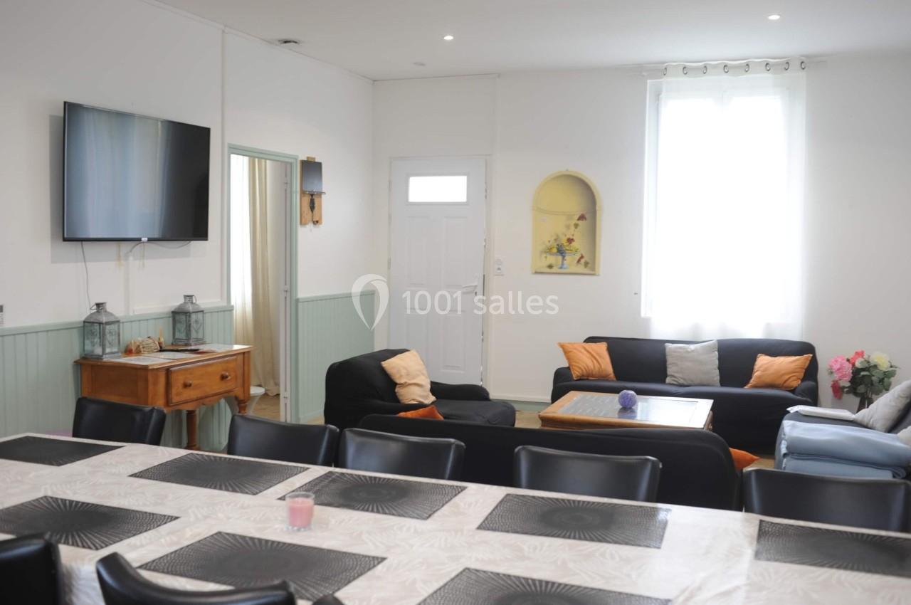 Salle de séjour lumineuse avec table à manger, canapés noirs et décoration sobre.