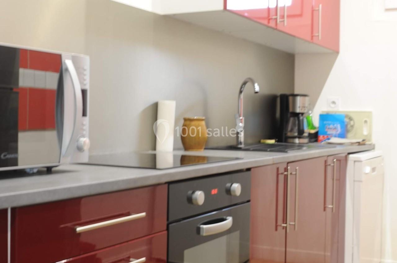 Cuisine moderne avec meubles rouges brillants, four encastré, micro-ondes, évier, cafetière et lave-vaisselle.