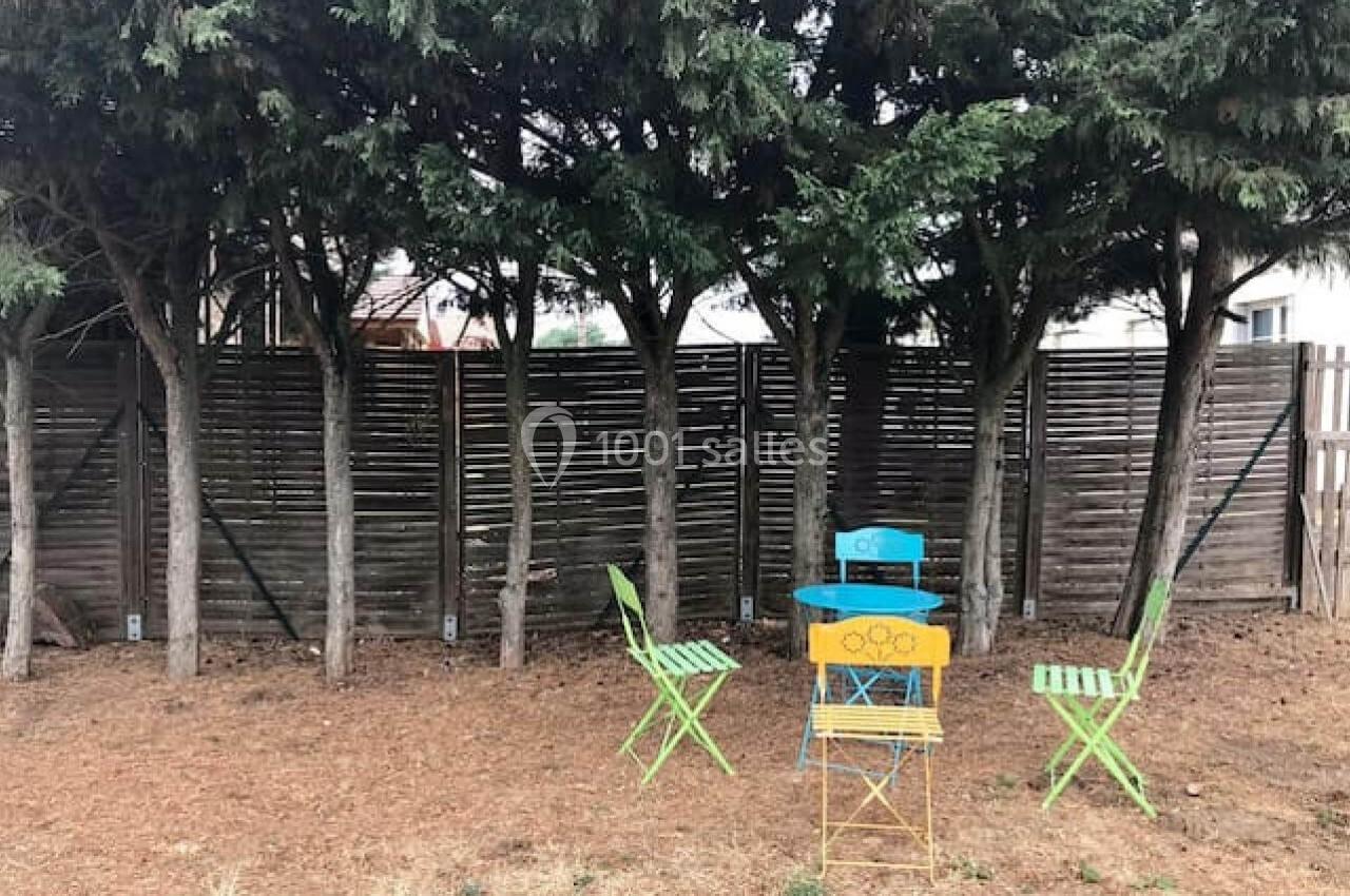 Deux chaises vertes et une table bleue sont disposées sous des arbres devant une clôture en bois.