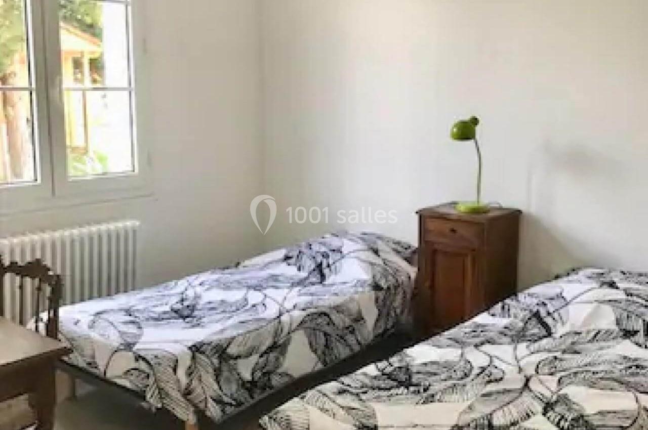 Deux lits simples avec housses à motifs noirs, une table de chevet avec lampe verte, dans une chambre lumineuse.