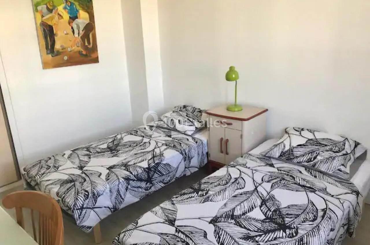 Deux lits simples avec des draps à motifs noirs, une table de chevet avec lampe verte et un tableau au mur.