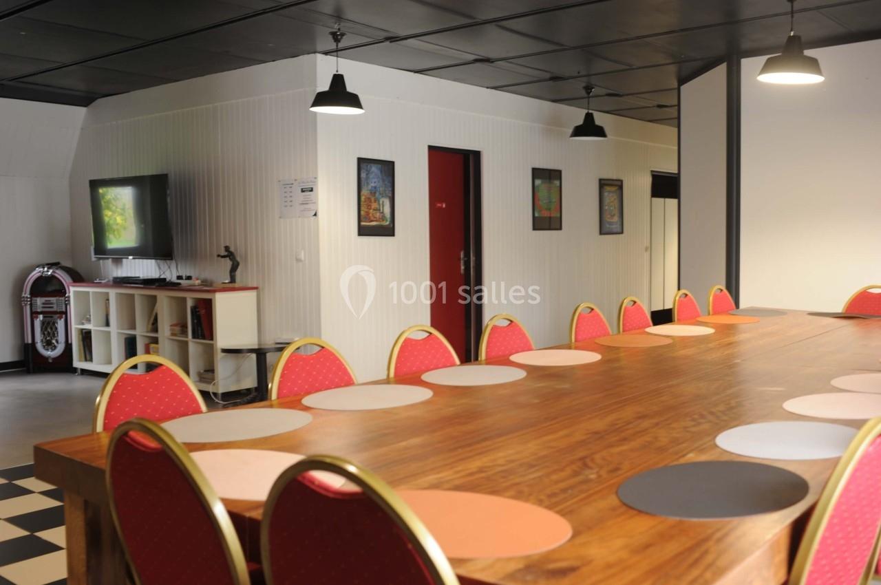 Grande table en bois entourée de chaises rouges dans une salle lumineuse avec décorations murales et éclairage suspendu.