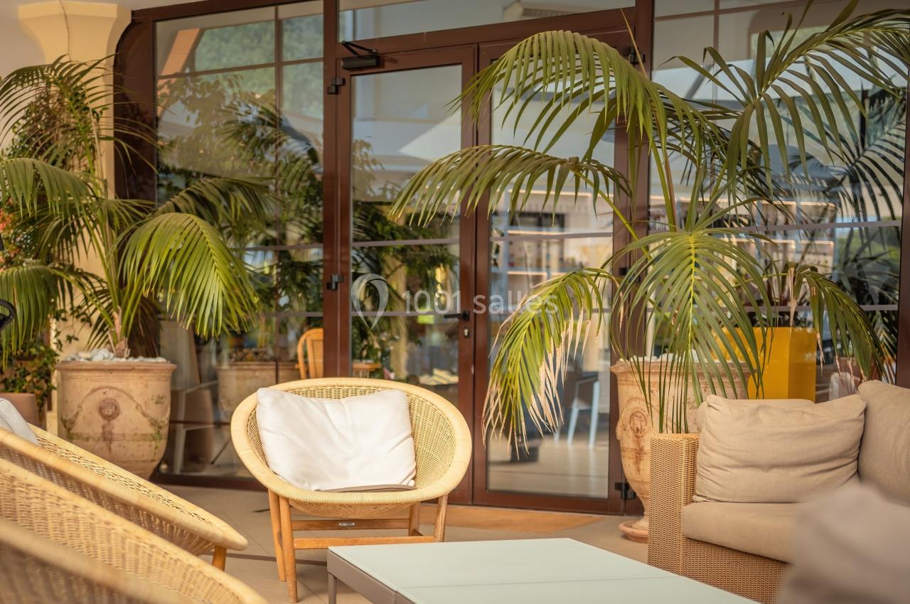 Espace de détente avec fauteuils en rotin, table basse et plantes tropicales devant une baie vitrée.