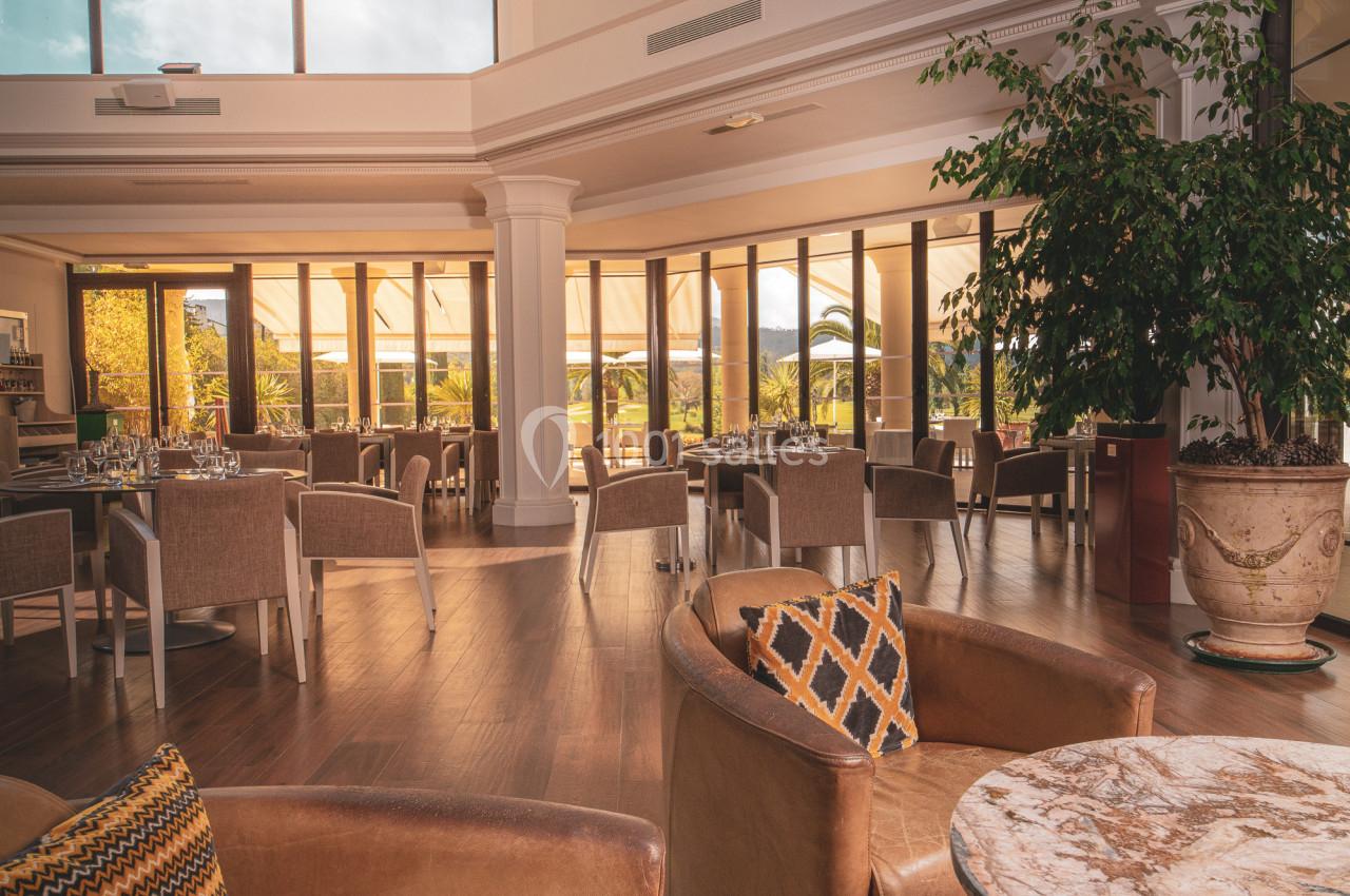 Salle lumineuse avec de grandes baies vitrées, mobilier en cuir et bois, et une horloge murale décorative.