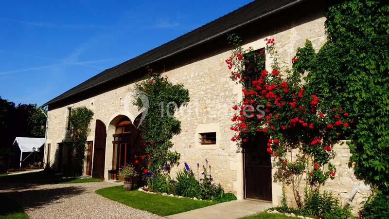 Façade en pierre d'une maison avec des rosiers grimpants rouges et un chemin gravillonné bordé de verdure.