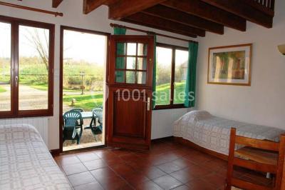 Chambre lumineuse avec deux lits simples, sol en carrelage, plafond en bois, et vue sur un jardin depuis une porte ouverte.