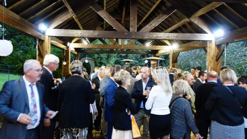 Groupe de personnes rassemblées sous une structure en bois, discutant lors d'un événement en extérieur.