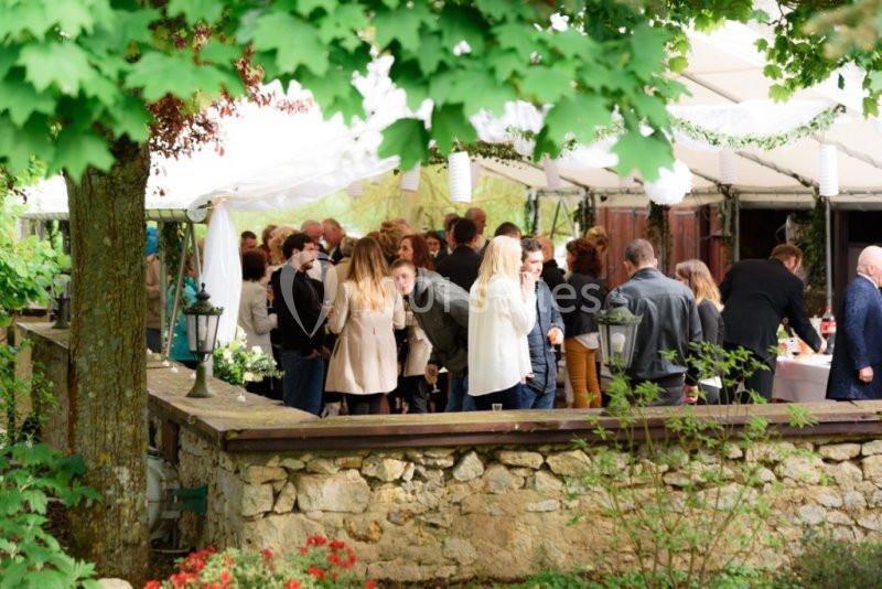 Groupe de personnes réunies dans un jardin sous une tente, entourées de verdure et de fleurs.