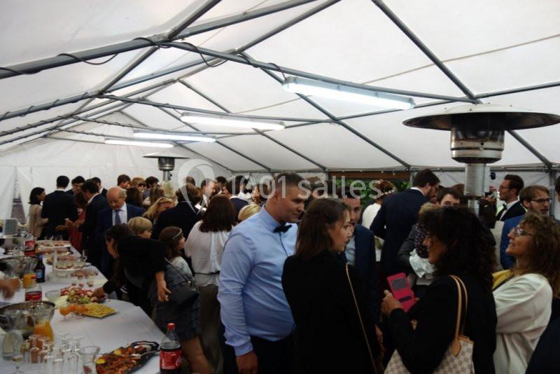 Groupe de personnes discutant sous une tente lors d'un événement, avec des tables de buffet en arrière-plan.