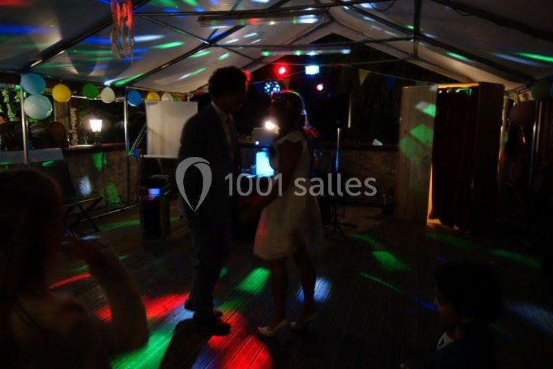 Un couple danse sous une tente éclairée par des lumières colorées lors d'une fête en soirée.