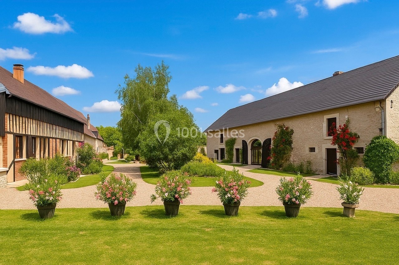 Cour intérieure avec pelouse, pots de fleurs alignés, bâtiments en pierre et bois, et arbres sous un ciel bleu.
