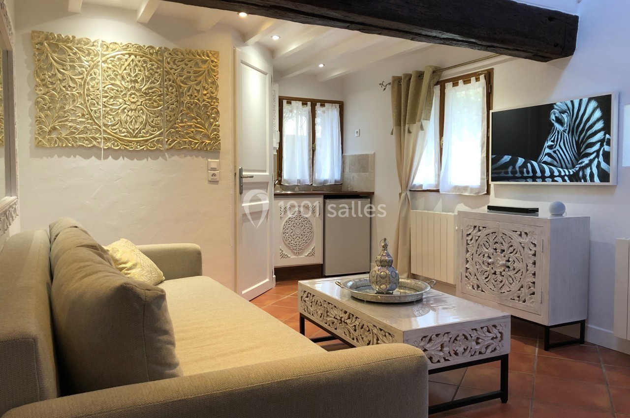 Salon lumineux avec canapé beige, table basse sculptée, télévision murale et décoration en bois ajouré.