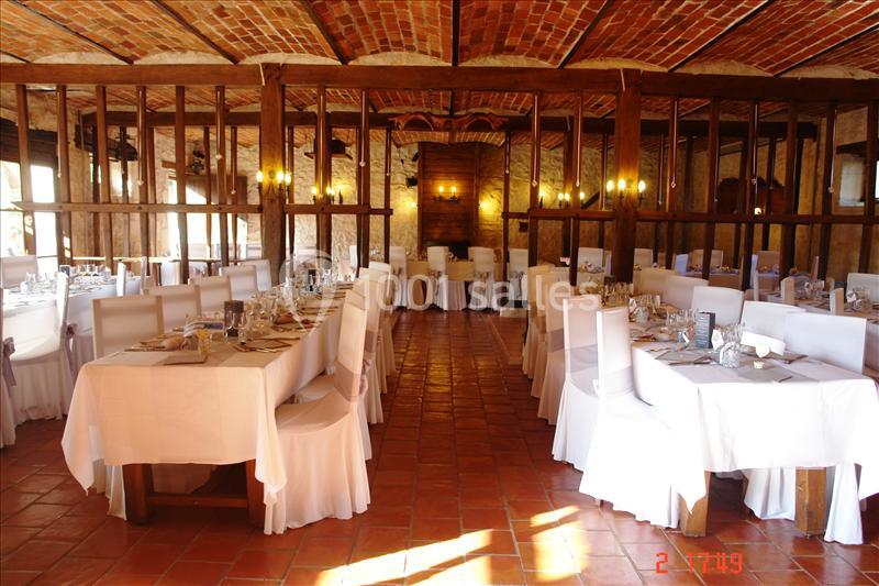 Salle de réception avec tables dressées, nappes blanches et plafond en briques apparentes.