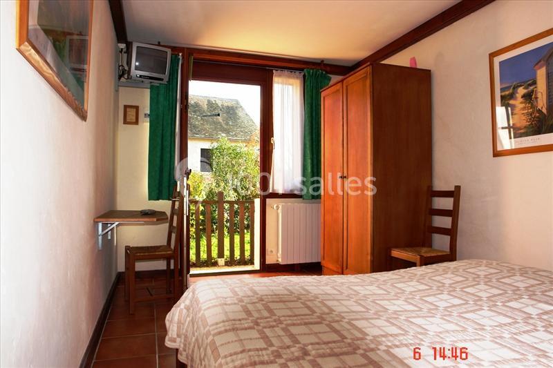 Chambre simple avec lit, armoire, bureau, télévision, et vue sur un jardin à travers une porte-fenêtre.