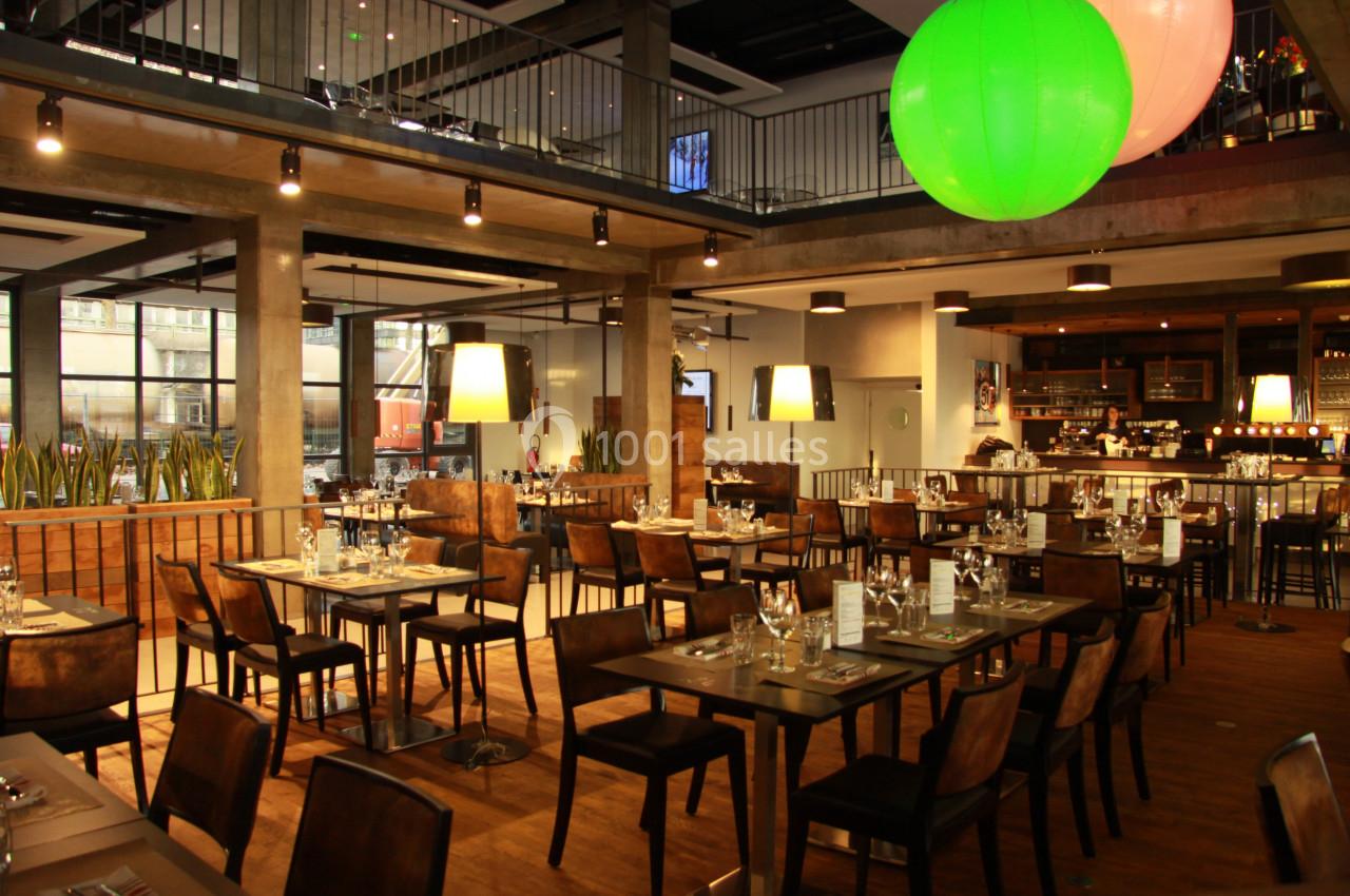 Salle de restaurant moderne avec tables dressées, éclairage chaleureux et grandes baies vitrées.