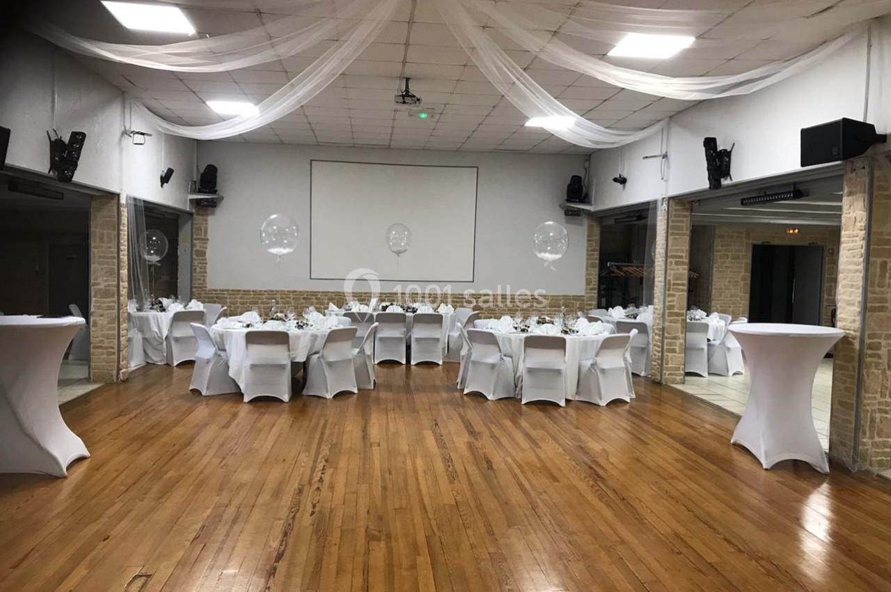 Salle de réception avec tables rondes dressées, nappes blanches et décoration sobre sous un plafond voilé.
