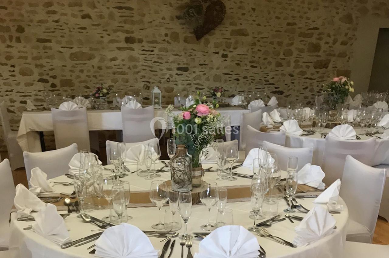 Salle de réception décorée avec des tables rondes dressées, nappes blanches et centres de table fleuris.
