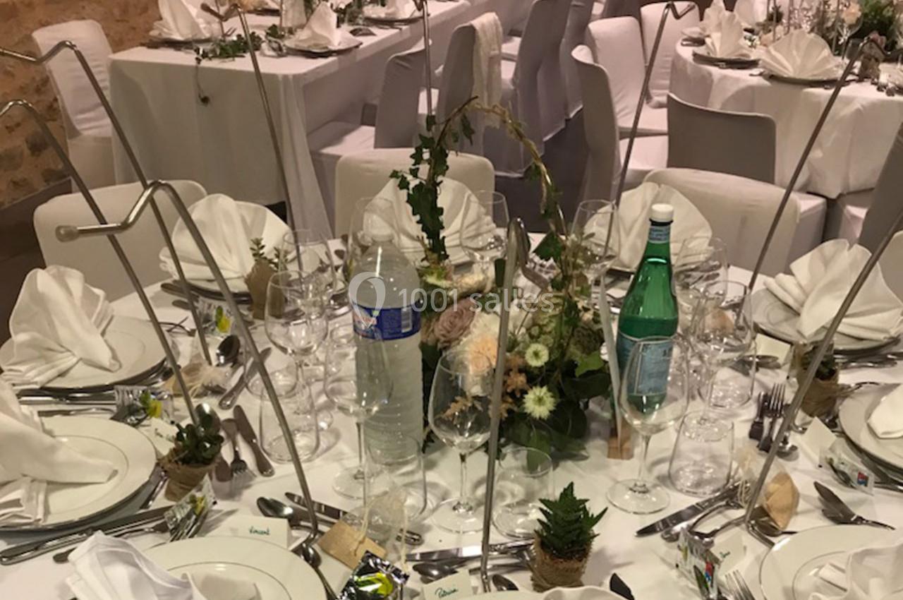 Table de réception élégamment dressée avec nappes blanches, vaisselle, serviettes pliées et décoration florale.