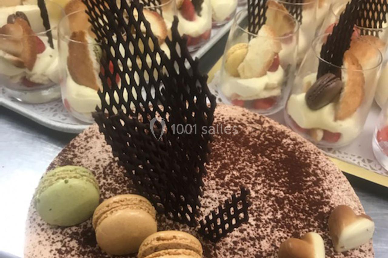 Gâteau décoré de macarons, cœurs en chocolat et grille en chocolat, entouré de verrines de desserts.