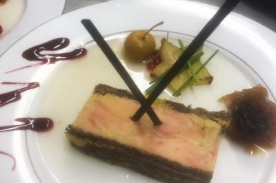 Tranche de foie gras en millefeuille avec décoration de fruits, sauce rouge et bâtonnets en chocolat.