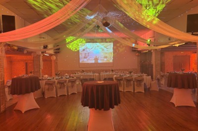 Salle de réception décorée avec des tables rondes dressées, éclairage rose et chaises blanches.