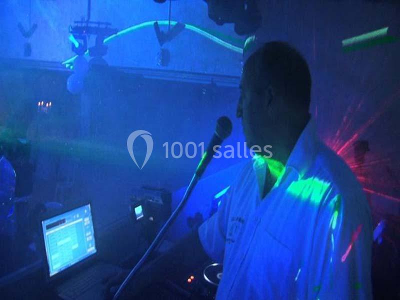 Homme en chemise blanche parlant dans un micro, éclairé par des lumières colorées dans une ambiance de fête.