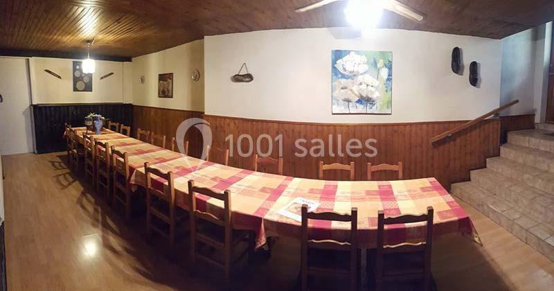 Grande table rectangulaire avec nappes colorées entourée de chaises en bois dans une salle au plafond lambrissé.