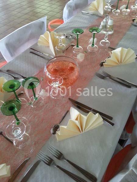 Table dressée avec nappes blanches, serviettes pliées en éventail, verres à pied verts et décoration centrale.