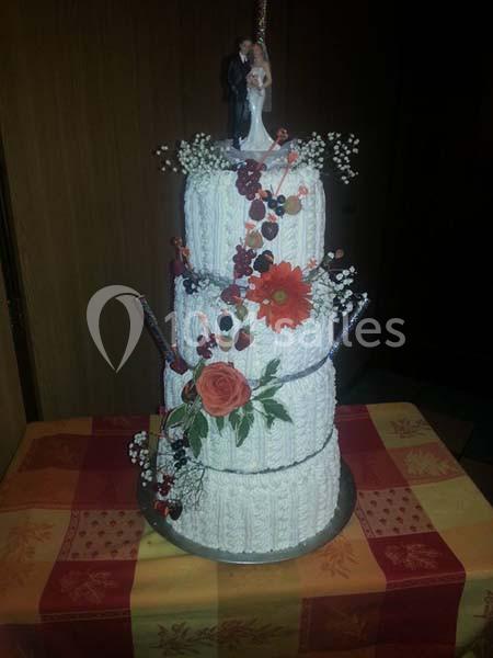 Gâteau de mariage à trois étages décoré de fleurs rouges, baies et figurines de mariés au sommet.
