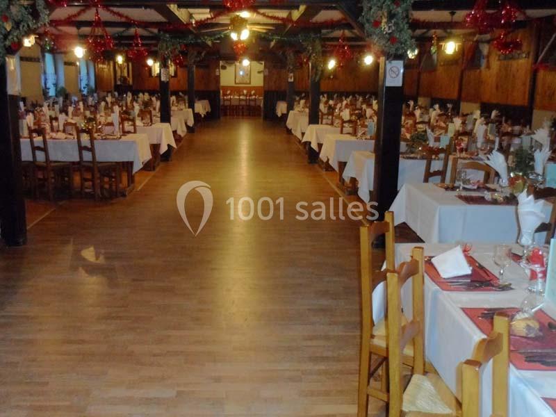 Salle de réception décorée pour un événement, avec des tables dressées et des chaises en bois alignées.