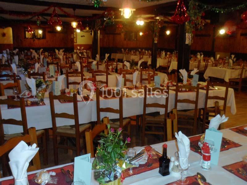 Salle de réception décorée avec des tables dressées pour un repas festif, ornées de nappes blanches et de décorations.