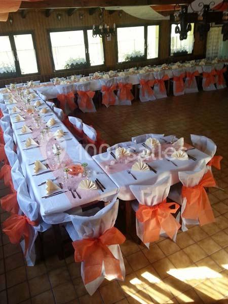 Salle de réception avec tables décorées de nappes blanches, chemins de table roses et chaises ornées de nœuds orange.