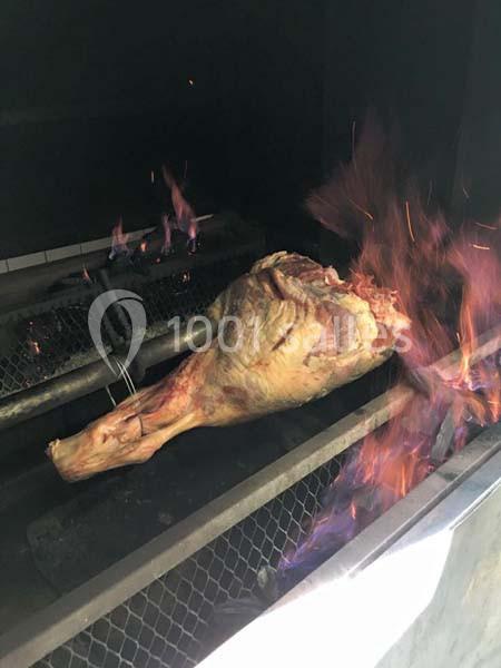 Morceau de viande entière en train de cuire sur un gril avec des flammes visibles.