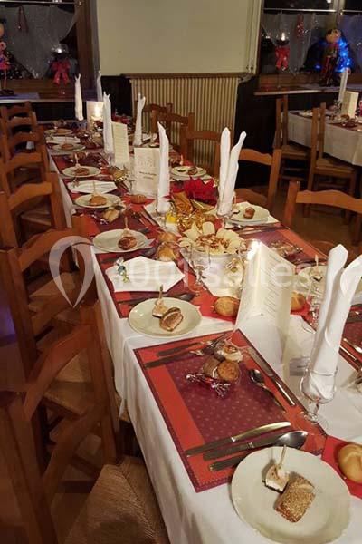 Table dressée pour un repas festif avec nappes blanches, serviettes pliées, menus et assiettes garnies.