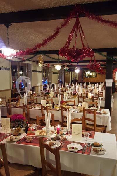 Salle de restaurant décorée pour les fêtes, avec tables dressées, nappes blanches et guirlandes suspendues.