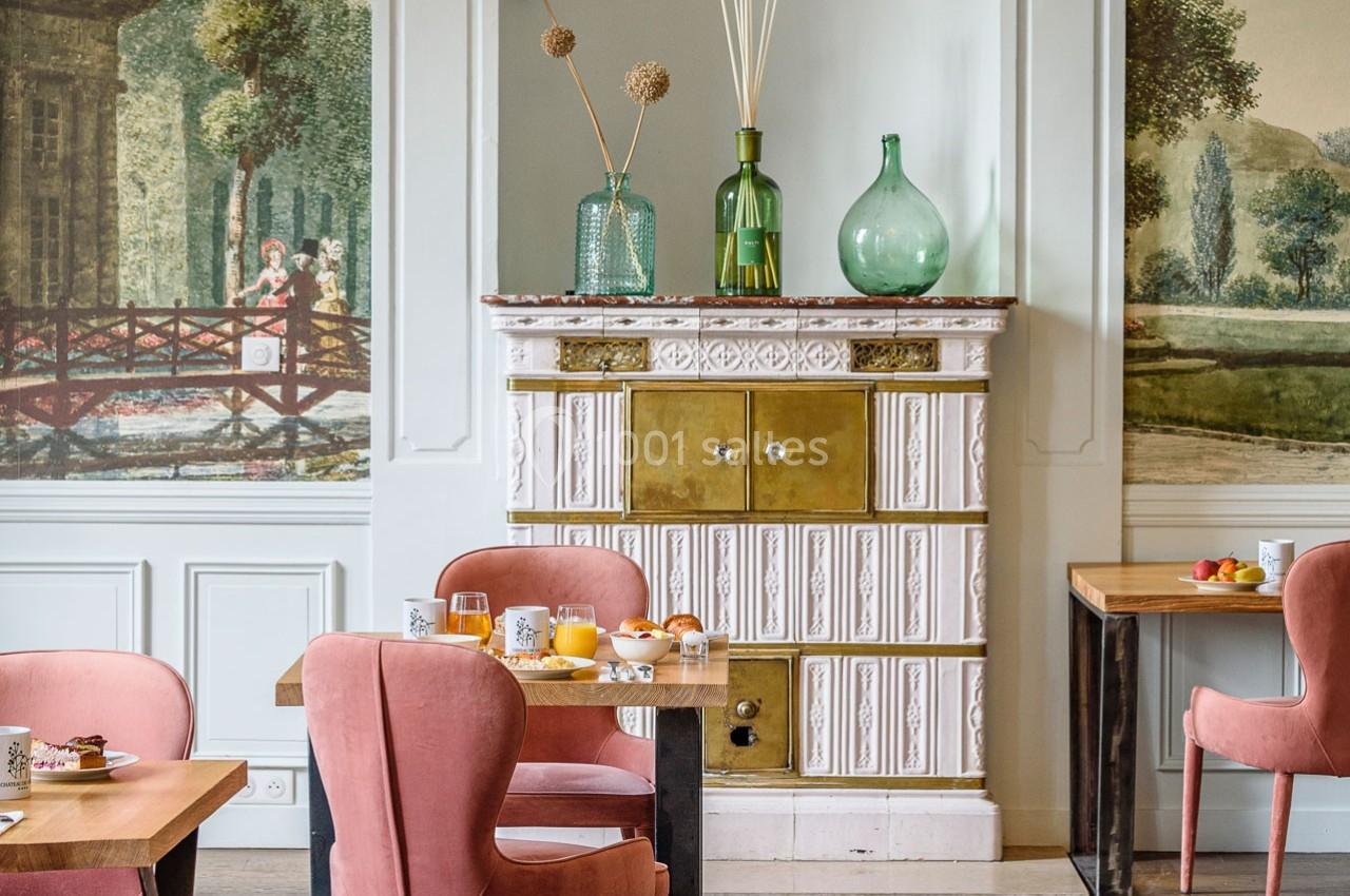 Salle à manger élégante avec des chaises roses, une cheminée ancienne et des tables dressées pour le petit-déjeuner.