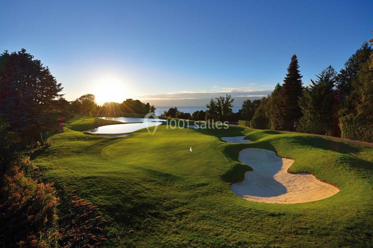 Paysage de golf au lever du soleil avec un green, des bunkers, des étendues d'eau et des arbres en arrière-plan.