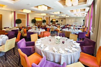Salle lumineuse avec une grande table dressée, plafond végétalisé, canapés colorés et équipements de détente.
