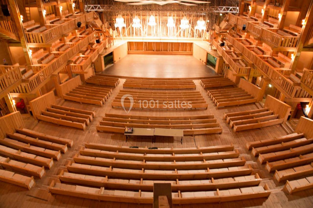 Salle de théâtre en bois avec des gradins vides et une scène éclairée en arrière-plan.