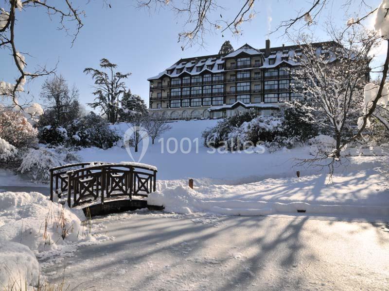Hôtel entouré de neige avec un pont en bois traversant un étang gelé au premier plan.