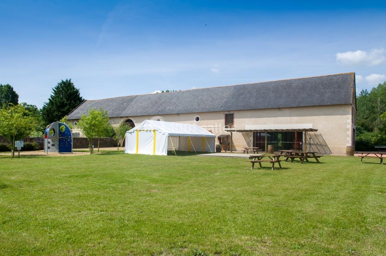 Grand espace extérieur avec pelouse, tables de pique-nique, barnum blanc et bâtiment en pierre sous un ciel dégagé.