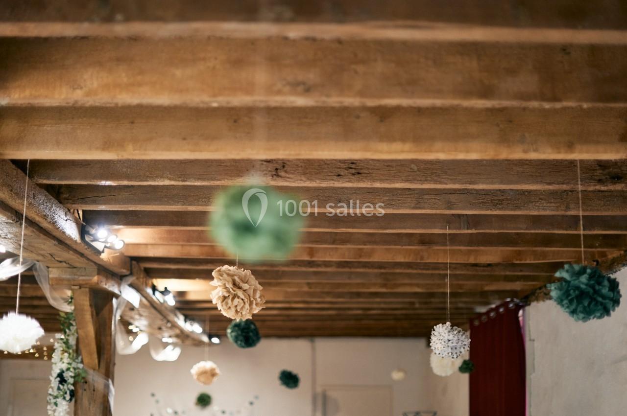 Plafond en bois avec des poutres apparentes, décoré de pompons suspendus dans des tons verts, blancs et beiges.