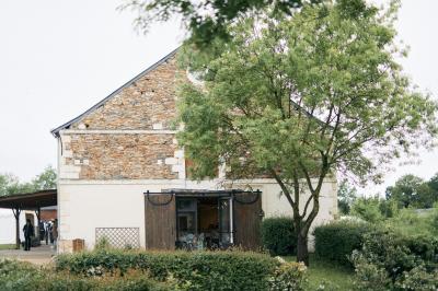 Chambre lumineuse avec lit double, rideaux transparents, plafond en poutres apparentes et vue sur une terrasse ensoleillée.