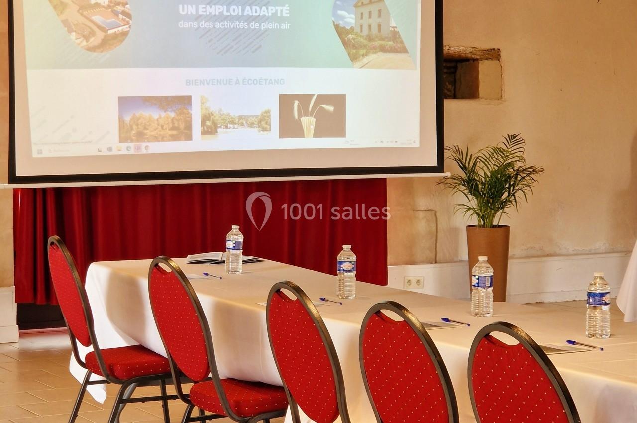 Salle de réunion avec des chaises rouges alignées, une table dressée et un écran de projection affichant un site web.