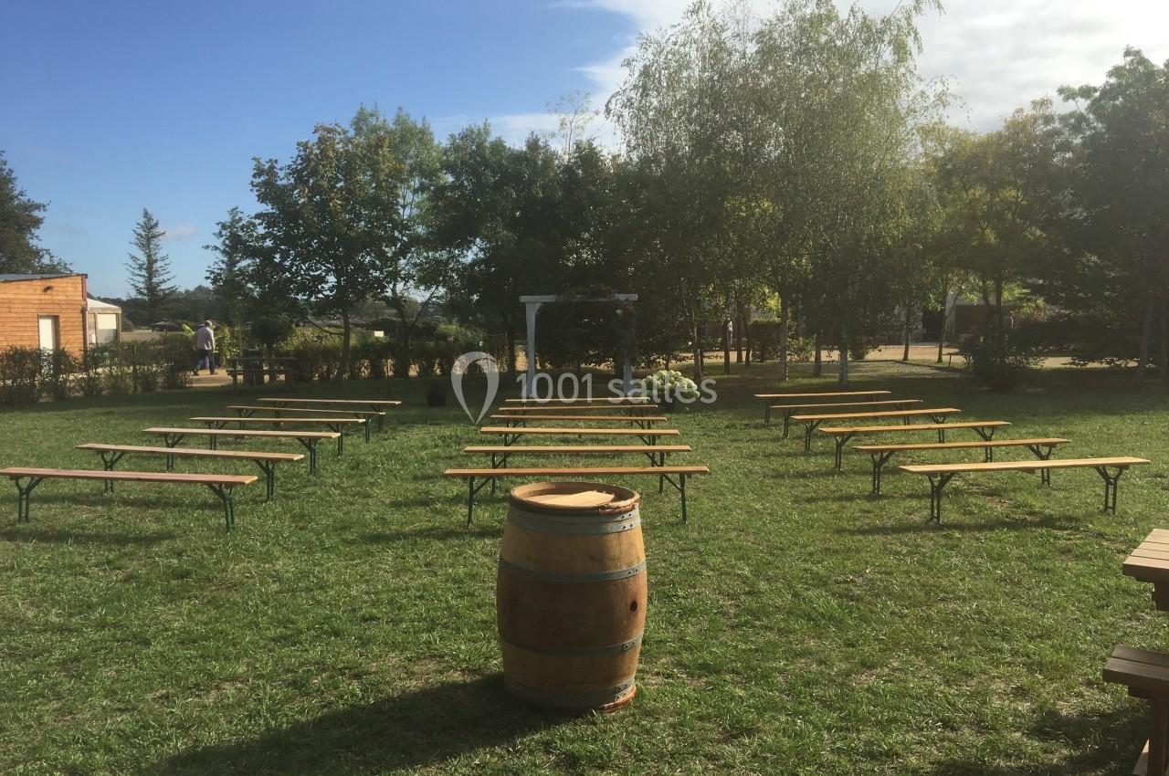 Alignement de bancs en bois sur une pelouse, avec un tonneau au premier plan et des arbres en arrière-plan.