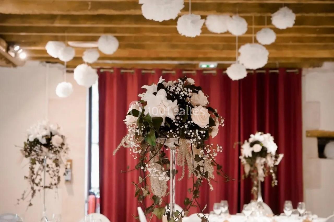 Salle de réception décorée avec des tables élégantes, centres de table floraux et suspensions blanches au plafond.