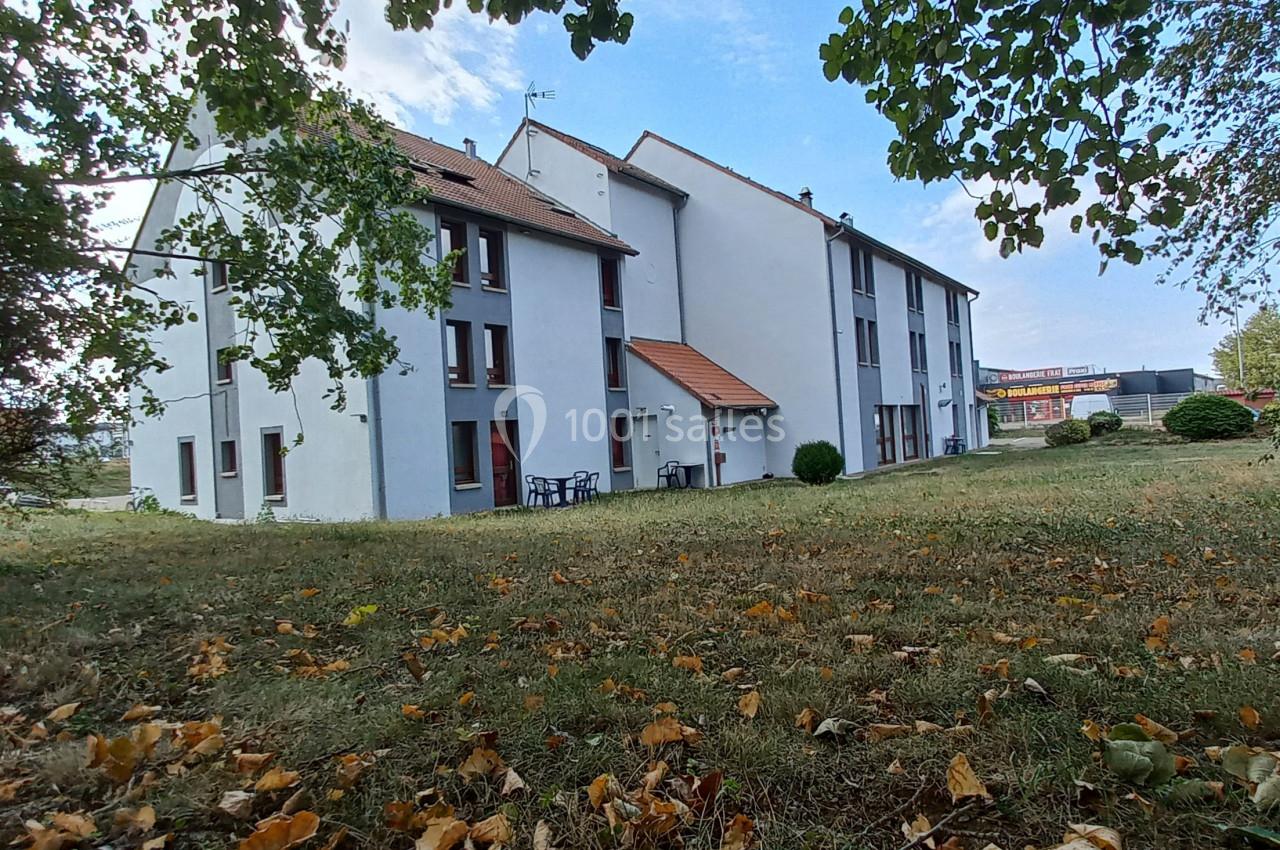 Bâtiment résidentiel blanc à plusieurs étages entouré d'un espace vert avec des arbres et des feuilles au sol.