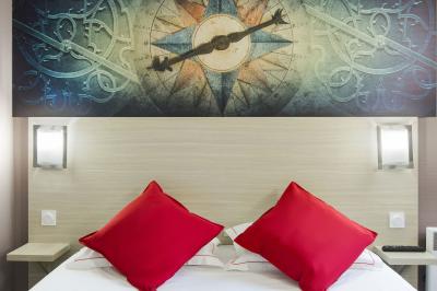 Lit avec deux coussins rouges, encadré par deux lampes murales, sous un tableau représentant une boussole.