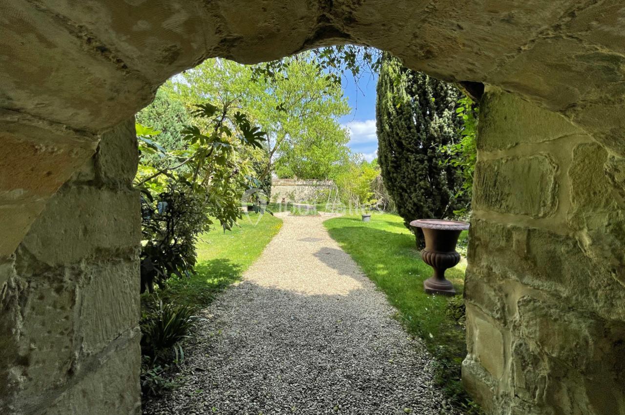 Vue d'un jardin verdoyant avec un chemin de gravier, encadrée par une arche en pierre.